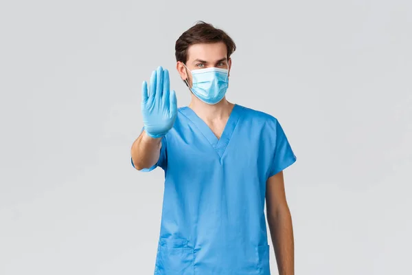 Coronavirus utbrott, vårdpersonal som bekämpar sjukdomar, sjukhus koncept. Självsäker läkare i medicinsk mask, blå skurar och handskar, visar stoppskylt, berätta tillräckligt eller sluta, förbjuda åtgärder — Stockfoto