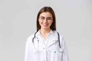 Sağlık çalışanları, ilaç, sigorta ve covid-19 salgını konsepti. Gülümseyen çekici kadın doktor, steteskop ve gözlüklü beyaz önlüklü doktor kameraya neşeli görünüyor.