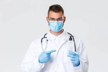 Covid-19, sağlık çalışanları, salgın hastalık ve virüs konsepti. Beyaz önlüklü, tıbbi maskeli, eldivenleri el dezenfektanını işaret eden ciddi İspanyol doktorlara sor.