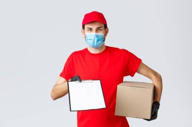 Paketler ve paket teslimatı, karantina teslimatı, nakil emirleri. Kırmızı üniformalı arkadaş canlısı kurye, yüz maskesi ve eldiven, paket kutusu ve dosya sipariş formunu istemciye ver
