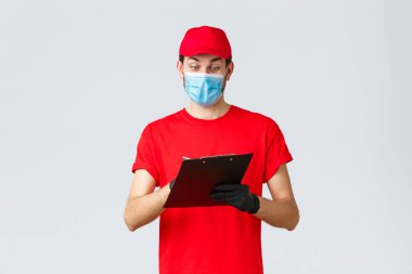 Paketler ve paket teslimatı, karantina teslimatı, nakil emirleri. Kırmızı üniformalı hevesli bir kurye, maske ve eldiven takıyor, not alıyor, sipariş formlarını kontrol ediyor, malları dağıtıyor.