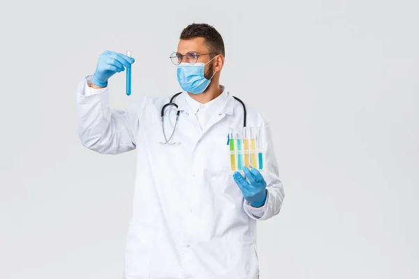 Covid-19, 의료 종사자, 전염병, 그리고 바이러스의 개념 방지. 하얀 수술복 과 의료 마스크를 입은 재능있는 의사나 실험실의 진료소 직원, 시험관을 보고, 샘플을 연구하고, 백신 연구를 하고, — 스톡 사진