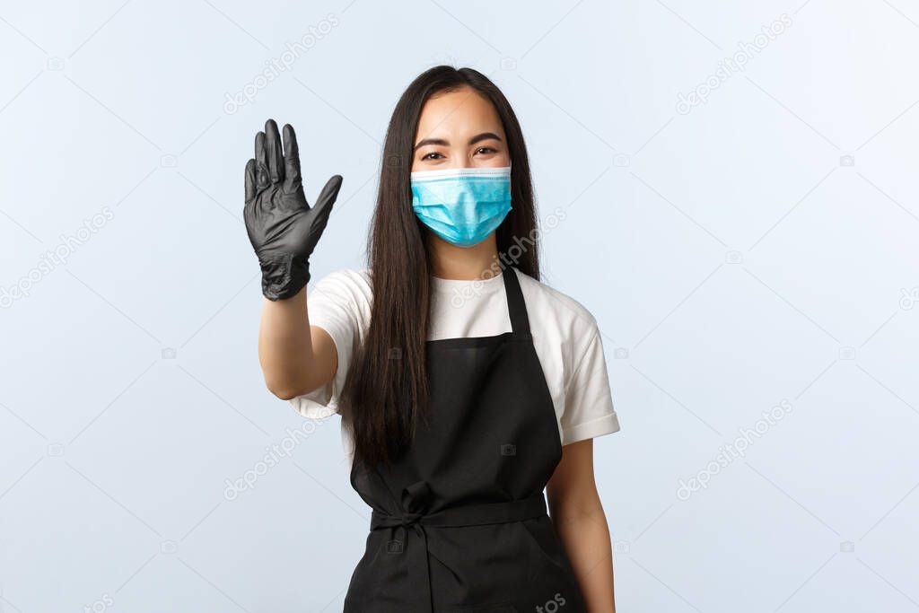 Covid-19, social distancing, small coffee shop business and preventing virus concept. Cheerful and friendly smiling asian female barista, waitress saying hi to visitors, waving hand in hello