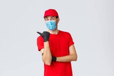 Covid-19, kendini karantina, online alışveriş ve nakliye konsepti. Kırmızı üniformalı, maskeli, eldivenli, soldaki tanıtımda müşterilere ikramiye ya da uygulama gösteren heyecanlı teslimatçı.