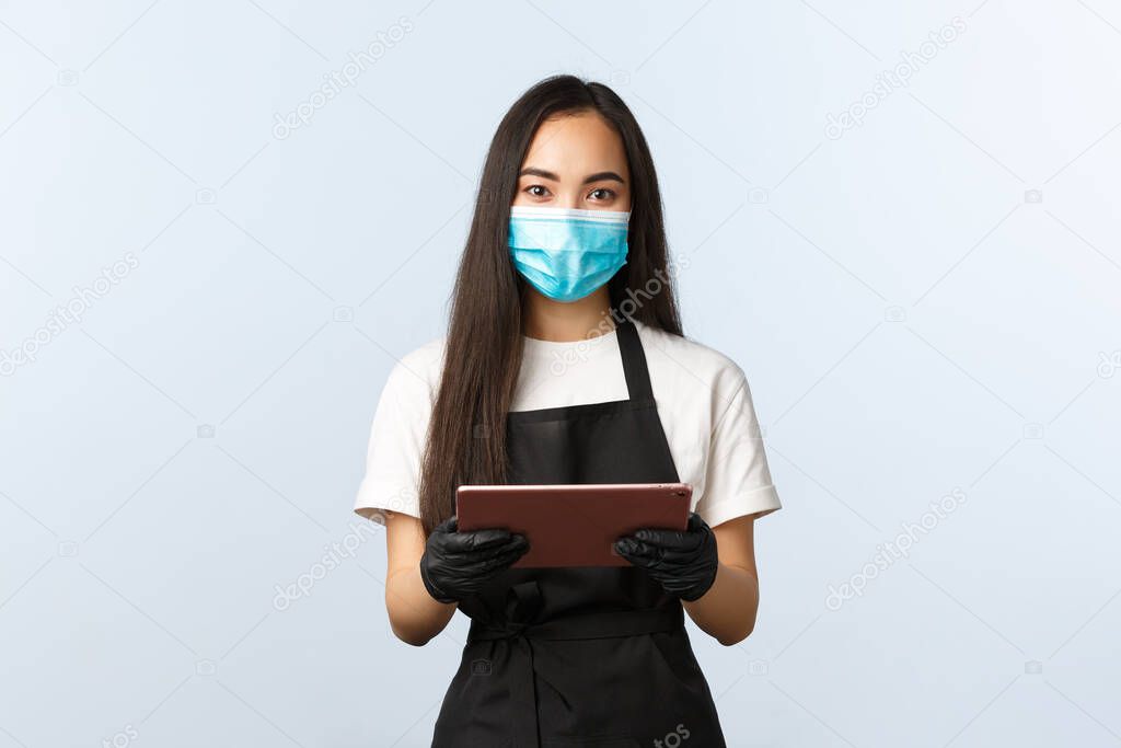 Covid-19, online orders, small coffee shop business and preventing virus concept. Friendly-looking asian female barista ready take your order, wear medical mask and gloves, hold digital tablet