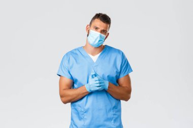 Sağlık çalışanları, covid-19, koronavirüs ve virüs konseptini önlemek. Yakışıklı, yorgun doktor, sağlık maskeli erkek hemşire ve önlüklü, çatlak parmaklı ve kamera yorgun, gri arka planda.