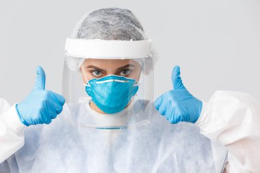 Covid-19, virüsün önlenmesi, sağlık, sağlık çalışanları ve karantina konsepti. Kendine güvenen yakın doktor, kişisel koruyucu ekipman hemşiresi, baş parmak gösterme, hastane çalışanlarına inanma.