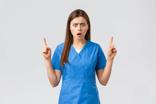 Trabajadores de la salud, prevenir virus, seguros y concepto de medicina. Dios mío, esto. Enfermera o médico sorprendido y preocupado en uniformes azules, enojado frunciendo el ceño, jadeando señalando con los dedos hacia arriba — Foto de Stock