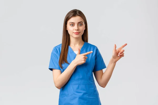 Trabajadores de la salud, prevenir virus, seguros y concepto de medicina. Enfermera o médico joven en uniformes azules que señalan con los dedos a la derecha, recomiendan pancarta o promo para pacientes de la clínica — Foto de Stock