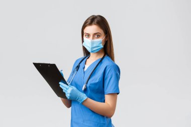 Covid-19, virüsün önlenmesi, sağlık, sağlık çalışanları ve karantina konsepti. Profesyonel kadın hemşire ya da doktor mavi önlüklü, tıbbi maske ve eldivenli hasta bilgilerini not alıyor.