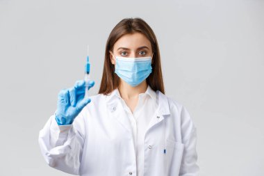 Covid-19, virüsü önleme, sağlık çalışanları ve karantina konsepti. Tıbbi maske ve lastik eldiven takmış kararlı profesyonel bir doktor. Coronavirus aşısı dolu bir şırınga gösteriyor.