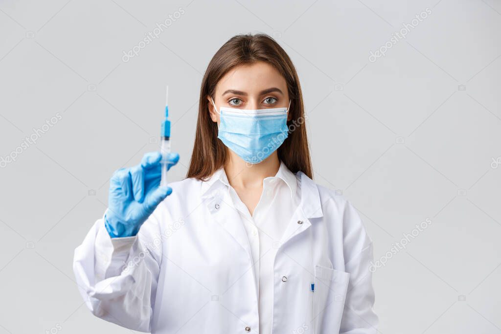 Covid-19, preventing virus, healthcare workers and quarantine concept. Determined professional doctor in medical mask and rubber gloves, showing syringe filled with coronavirus vaccine