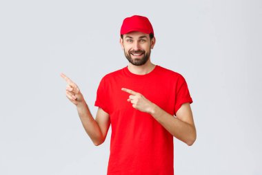 İnternetten alışveriş, karantina sırasında teslimat ve paket servis konsepti. Arkadaş canlısı yakışıklı sakallı çalışan, kırmızı üniformalı kurye ve tişört giyen, sol elini gösteren, müşteriyi davet eden...