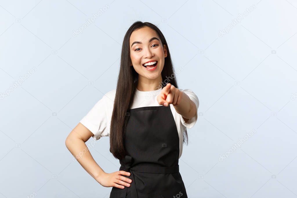 Coffee shop, small business and startup concept. Cheerful friendly asian barista or restaurant employee, smiling and pointing finger at camera, inviting come to cafe, white background