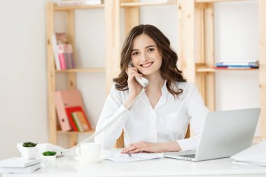 Modern ofiste telefonla konuşan genç bir kadın..