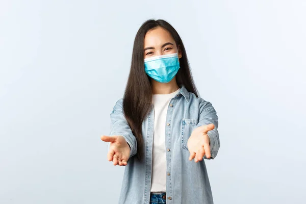 Social distancing lifestyle, covid-19 pandemic everyday life and leisure concept. Friendly lovely asian woman in medical mask reaching hands forward to take something or hold, white background — Stock Photo, Image