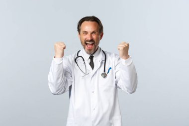 Covid-19, koronavirüs salgını, sağlık çalışanları ve pandemik konsept. Heyecanlı erkek doktor kazanıyor, iyi haberler alıyor, yumruk tokuşturarak ilahi söylüyor, evet seviniyor, başarıyı kutluyor.
