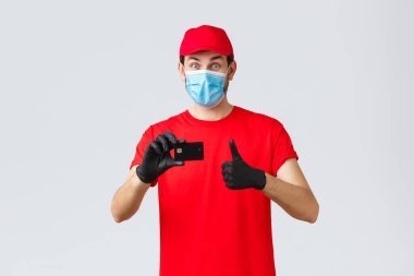 Bağlantı kurulamayan teslimat, ödeme ve kovid 19 sırasında online alışveriş, kendini karantina. Kırmızı t-shirt ve şapka üniformalı mutlu kurye, eldivenli yüz maskesi, kredi kartı siparişi ödeme önerisi