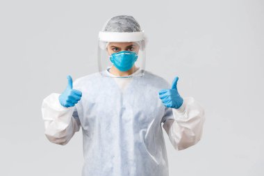 Covid-19, virüsün önlenmesi, sağlık, sağlık çalışanları ve karantina konsepti. Kararlı, kendine güvenen doktor, koruyucu ekipman hemşiresi, solunum cihazı ve eldivenler, baş parmağınızı kaldırın, Corona 'yla savaşın.