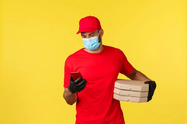 Food delivery, tracking orders, covid-19 and self-quarantine concept. Courier checking client adress on phone as bring pizza order, calling customer, standing yellow background — Stock Photo, Image
