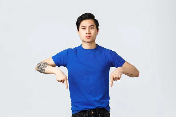 Diferentes emoções, estilo de vida das pessoas e conceito de publicidade. Sério e confiante asiático homem em azul t-shirt, apontando os dedos para baixo e olhando câmera determinada, informar sobre notícias — Fotografia de Stock