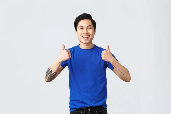 Diferentes emoções, estilo de vida das pessoas e conceito de publicidade. Upbeat bonito asiático homem em azul t-shirt, sendo solidário mostrando polegar-up na aprovação, recomendar ou garantir o produto — Fotografia de Stock