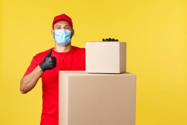 Salgın sırasında hızlı teslimat, covid-19, güvenli nakliye, online alışveriş konsepti. Gururlu ve kendinden emin kurye paketlerin güvende olduğunu garanti ediyor. Paketlerin olduğu kutuların yanında duruyor.