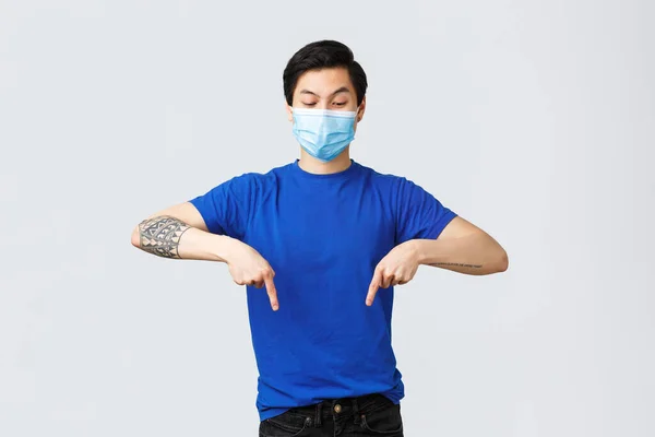 Olika känslor, social distans, självkarantän på coronavirus och livsstil koncept. Spännande och fascinerad asiatisk man i medicinsk mask, pekar finger ner och tittar på banner nyfiken — Stockfoto