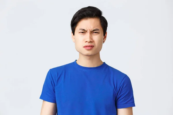 Lifestyle, people emotions and beauty concept. Wtf going on. Frustrated and puzzled asian guy in blue t-shirt frowning, grimacing confused cant understand what happened, stand grey background — Stock Photo, Image