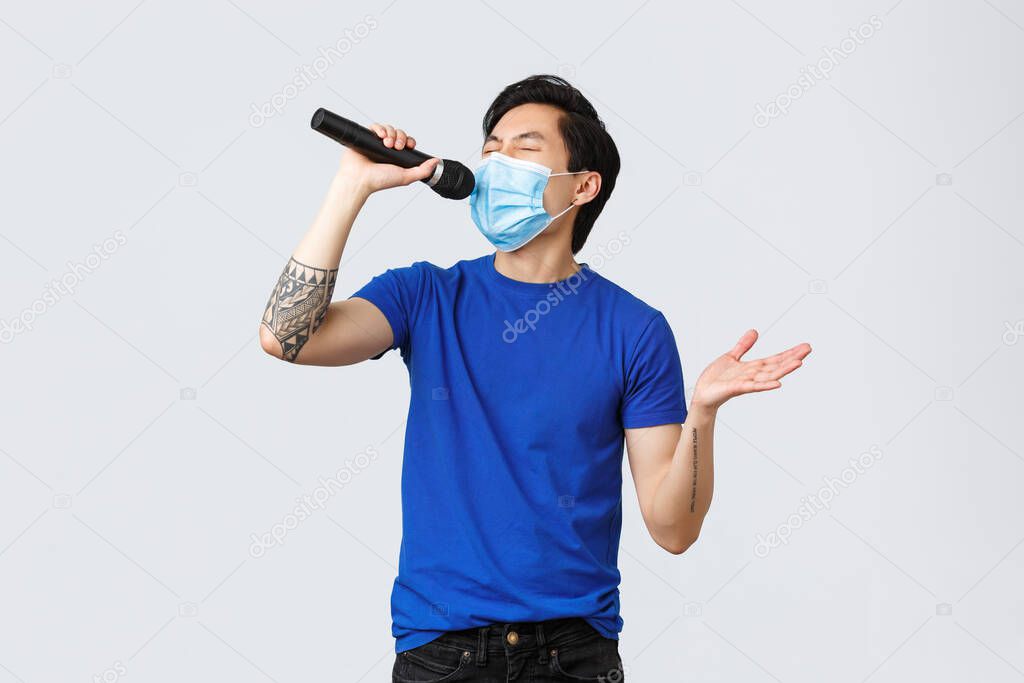 Covid-19 lifestyle, people emotions and leisure on quarantine concept. Handsome funny young male student staying home during coronavirus pandemic, wear mask and singing karaoke in microphone