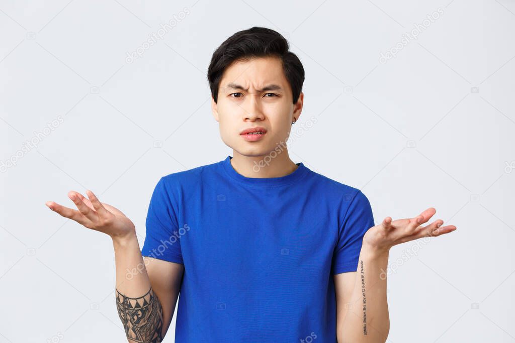 Lifestyle, people emotions and beauty concept. Confused and indecisive young asian man cant understand what happened, shrugging with hands spread and puzzled grimace,wear blue t-shirt