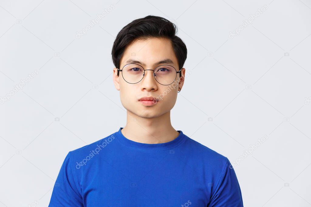 Lifestyle, people emotions and beauty concept. Close-up of asian man in glasses with stylish haircut looking at camera with normal, calm expression, standing grey background