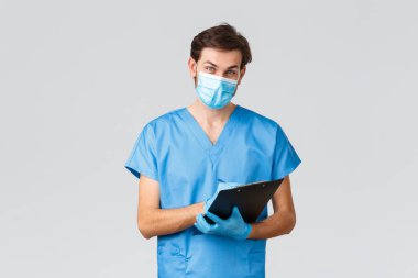 Covid-19, karantina, hastaneler ve sağlık çalışanları konsepti. Tıbbi maskeli, önlüklü ve eldivenli neşeli doktor, hastaya bakıyor, problem ve belirtileri dinliyor, not tahtasına yazıyor.