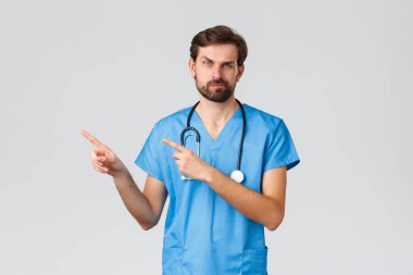 Sağlık çalışanları, salgın hastalık ve koronavirüs salgını konsepti. Sıkıntılı, huysuz, önlüklü, steteskoplu doktor. Sol üst köşeyi işaret ediyor, kaşlarını çatıyor ve hayal kırıklığına uğruyor.