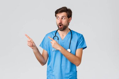 Sağlık çalışanları, salgın hastalık ve koronavirüs salgını konsepti. Mavi önlüklü, steteskoplu, düşük çeneli, soluk soluklu ve bakışlı heyecanlı ve şaşkın doktor reklamlara veya ilginç haberlere bakıyor