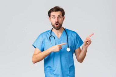 Sağlık çalışanları, salgın hastalık ve koronavirüs salgını konsepti. Heyecanlı ve şaşkın doktor şok edici haberleri görüyor, parmaklarını doğru gösteriyor, önlük giyiyor ve steteskop takıyor, hastayla sohbet ediyor.