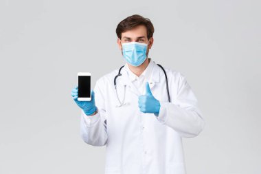 Hastane, sağlık çalışanları, covid-19 tedavi konsepti. Tıbbi maskeli, önlüklü ve eldivenli güvenilir profesyonel doktor tecrit sırasında hasta başvurusu akıllı telefonu ya da iletişim kurmak için uygulamayı gösteriyor.