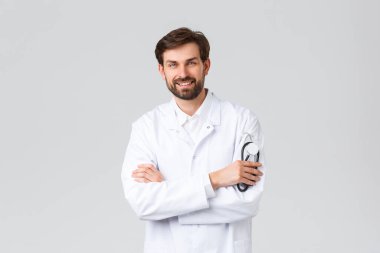 Hastane, sağlık çalışanları, covid-19 tedavi konsepti. Ameliyat önlüğü giymiş profesyonel bir doktor gülümsüyor, steteskop tutuyor, hastaları tedavi ediyor. Nöbeti sırasında klinikteki doktor.