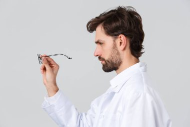 Hastane, sağlık çalışanları, covid-19 tedavi konsepti. Önlüklü ciddi görünümlü bir doktorun profil portresi, gözlüklere bakmak, hasta gözlüğü incelemek, hasta için gözlük seçen bir doktor.