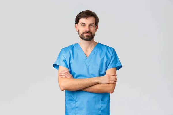 Trabajadores de la salud, campaña de cuarentena del coronavirus y concepto pandémico. Médico o enfermera de confianza en uniforme médico de matorrales azules, cámara sonriente en el pecho con las manos cruzadas, fondo gris — Foto de Stock