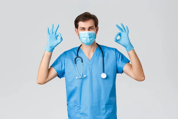 Εργάτες υγείας, εκστρατεία καραντίνας κορωναϊού και πανδημία. Χαμογελώντας όμορφος γιατρός σε scrubs, οικότροφος που εργάζεται με άρρωστους ασθενείς covid-19, καταπολέμηση της ασθένειας, δείχνουν εντάξει σημάδι, φορούν μάσκα — Φωτογραφία Αρχείου