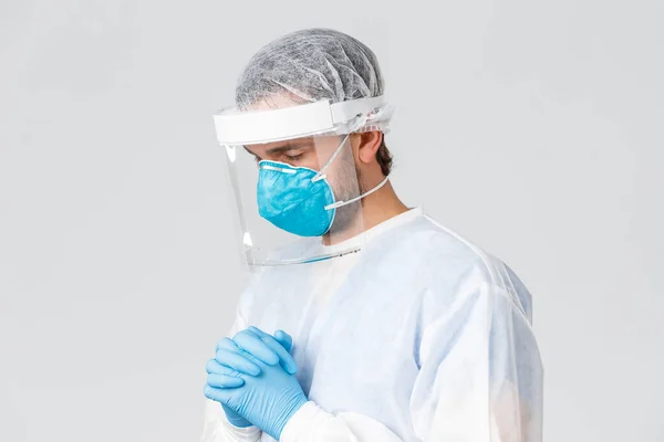 Covid-19, pandemic, healthcare workers fighting virus outbreak. Hopeful doctor in protective suit, gloves and medical mask having hope, praying God, close eyes pleading strength to tackle coronavirus — Stock Photo, Image
