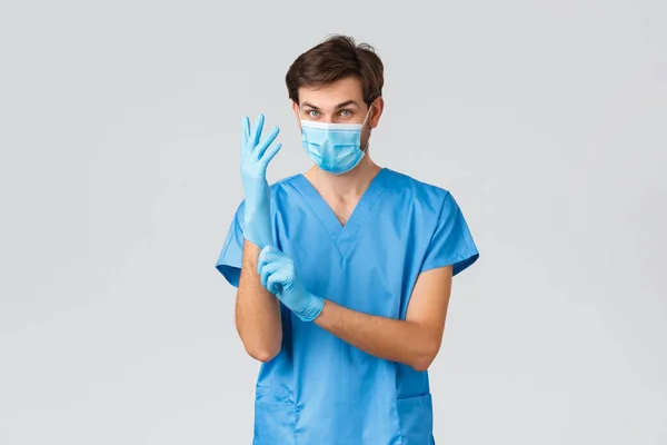 Covid-19, quarantine, hospitals and healthcare workers concept. Enthusiastic doctor treating patients in clinic, put on personal protective equipment before surgeon, gloves and medical mask — Stock Photo, Image