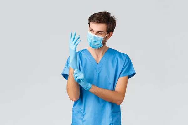 Covid-19, quarantine, hospitals and healthcare workers concept. Young doctor or physician put on rubber gloves, medical mask and scrubs before medical screening, examination of patient