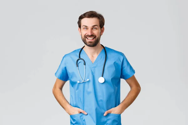 Ковид-19, карантин, больницы и медработники. Веселый улыбающийся врач или медсестра со стетоскопом и скрабами, дружелюбный разговор с коллегой или пациентом, серый фон — стоковое фото