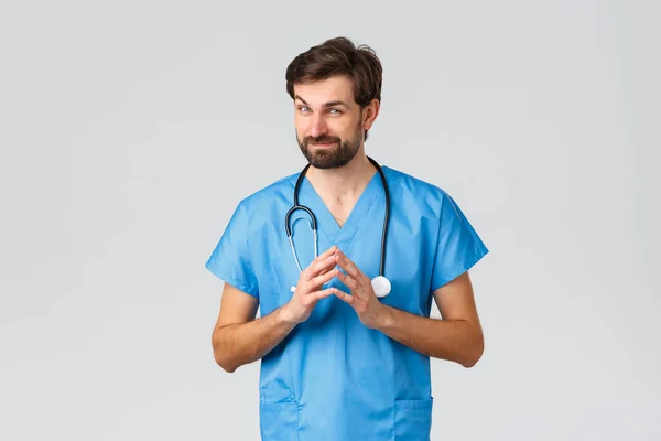 Covid-19, quarantine, hospitals and healthcare workers concept. Handsome professional doctor or nurse in scrubs, steeple fingers and smirk, talking to patient, have conversation, explain prescription — Stock Photo, Image