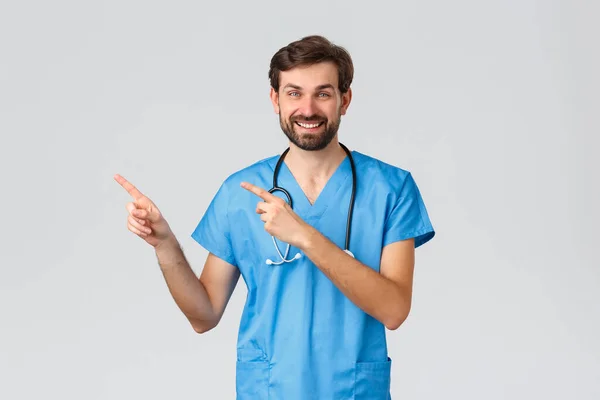 Covid-19, kwarantanna, szpitale i opieka zdrowotna. Lekarz w fartuchu, garnitur medyczny, wskazujący palcem górny lewy róg, uśmiechnięty aparat fotograficzny, promujący lub reklamujący leki lub usługi kliniczne — Zdjęcie stockowe
