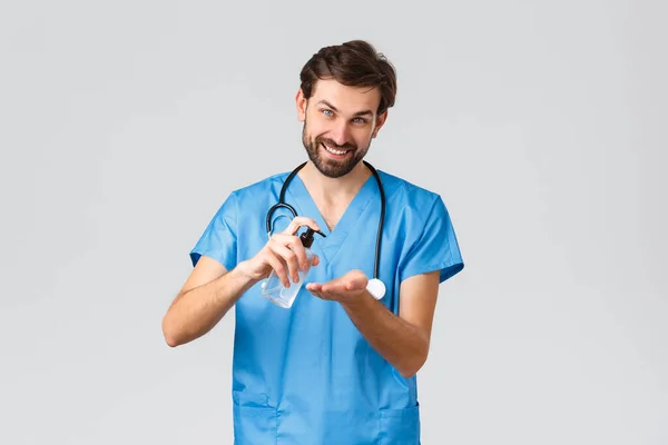 Gesundheitshelfer, Pandemie- und Coronavirus-Ausbruchskonzept. Lächelnder Mann, der zeigt, wie man Händedesinfektionsmittel benutzt, Seife auf die Handfläche tupft und Kamera anschaut, grauer Hintergrund — Stockfoto