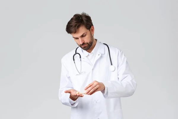 Hôpital, travailleurs de la santé, concept de traitement covid-19. Médecin sérieux en blouse blanche avec stéthoscope, pilules de comptage, médicaments à la main, regard concerné ou déterminé — Photo