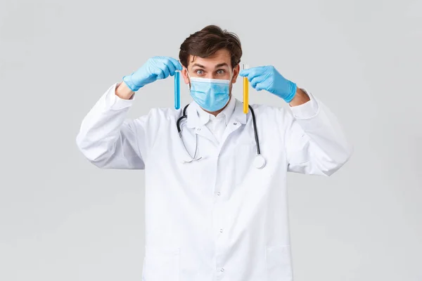 Hastane, sağlık çalışanları, covid-19 tedavi konsepti. Heyecanlı doktor, beyaz önlüklü laboratuar teknisyeni, orta maske ve eldivenli, kameraya bakarken koronavirüs aşısı bulundu, iki ampul gösteriyor. — Stok fotoğraf